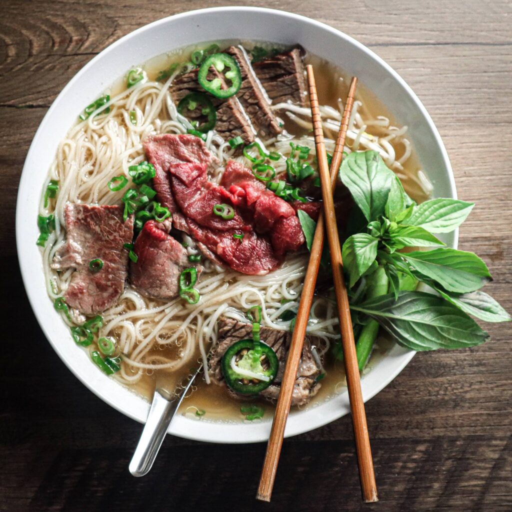 A bowl of Vietnamese pho plated with fresh green herbs and various cuts of beef.