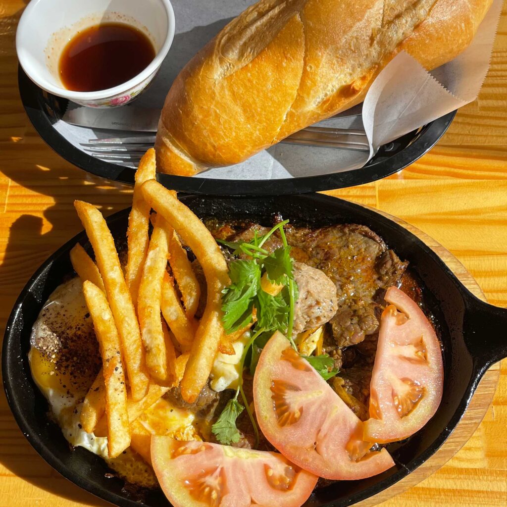 Vietnamese steak and eggs served on a hot skillet with a side of French bread.